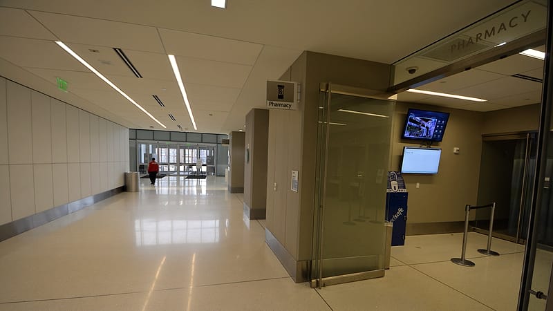 A clipboard resting on a stainless steel counter in a bright corridor, with a numbered door sign visible behind it.